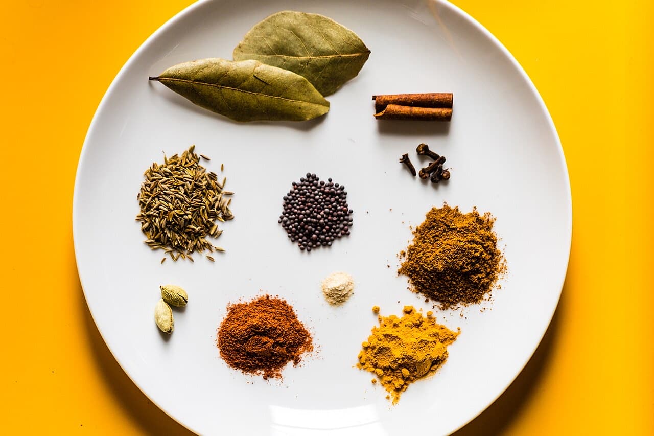 Whole and ground Indian spices arranged on a white plate