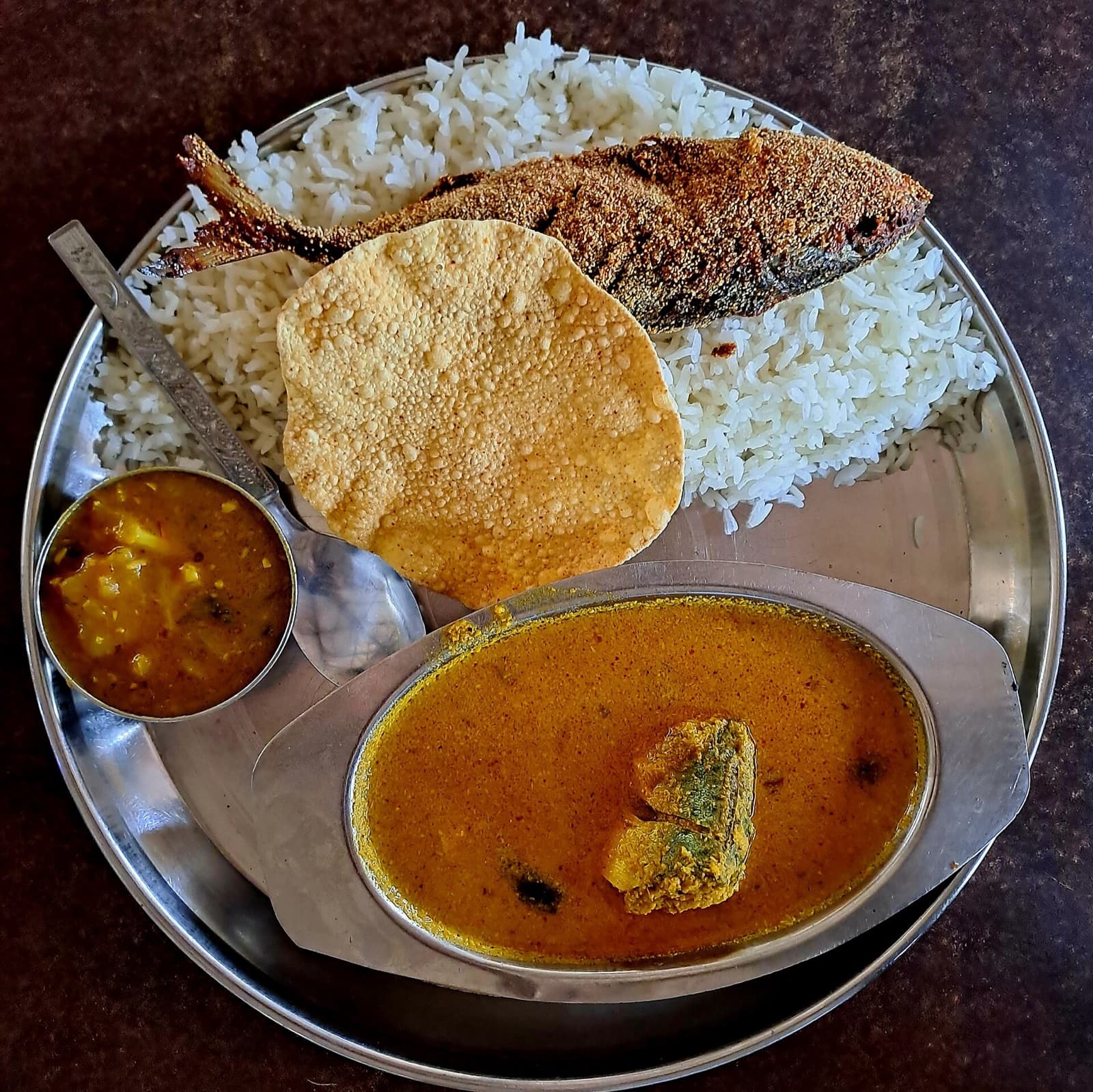 A Goan fish thali with fried fish, rice, a papad, a bowl of fish curry and a small vegetable side