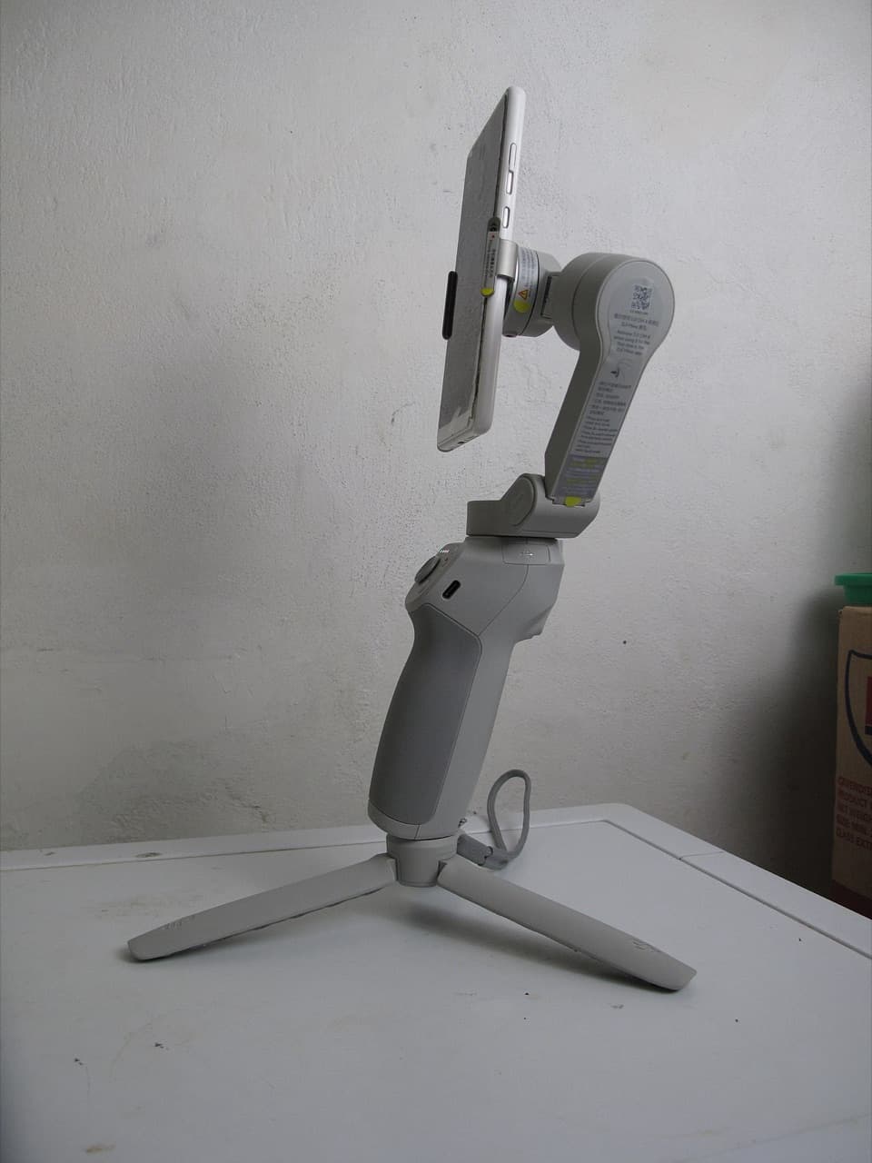 Side view of a DJI smartphone gimbal with a phone mounted, standing on its mini tripod