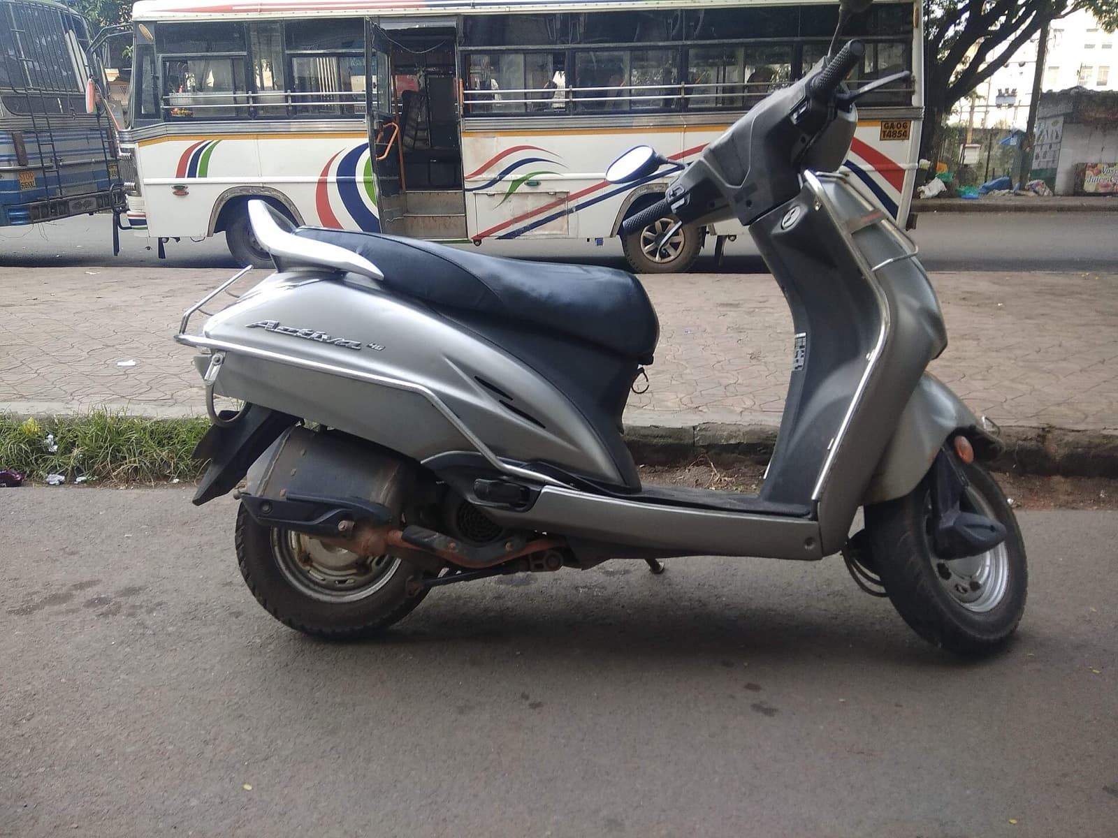Silver Honda scooter with a black seat parked on a roadside, a bus behind it