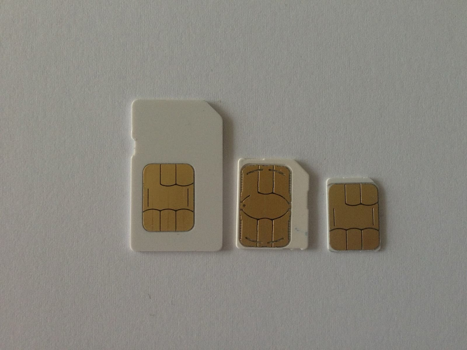 Three SIM cards of decreasing size, standard, micro and nano, laid side by side on a white surface