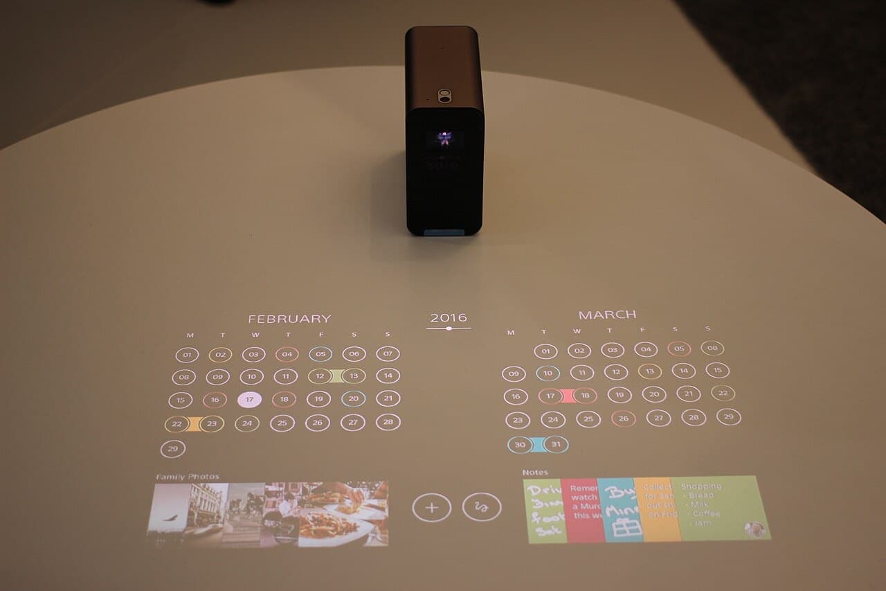 Small portable short-throw projector casting a calendar and photos onto a tabletop