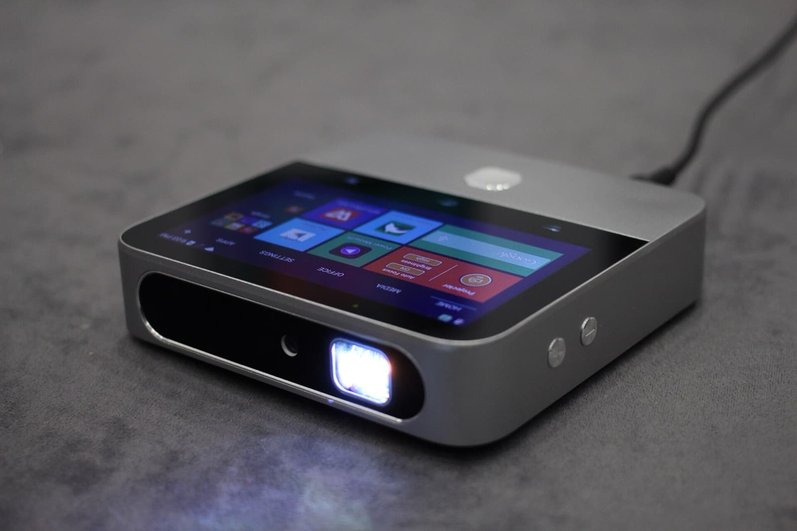 A compact ZTE smart projector with a touchscreen on top, its lens lit up, resting on a grey surface