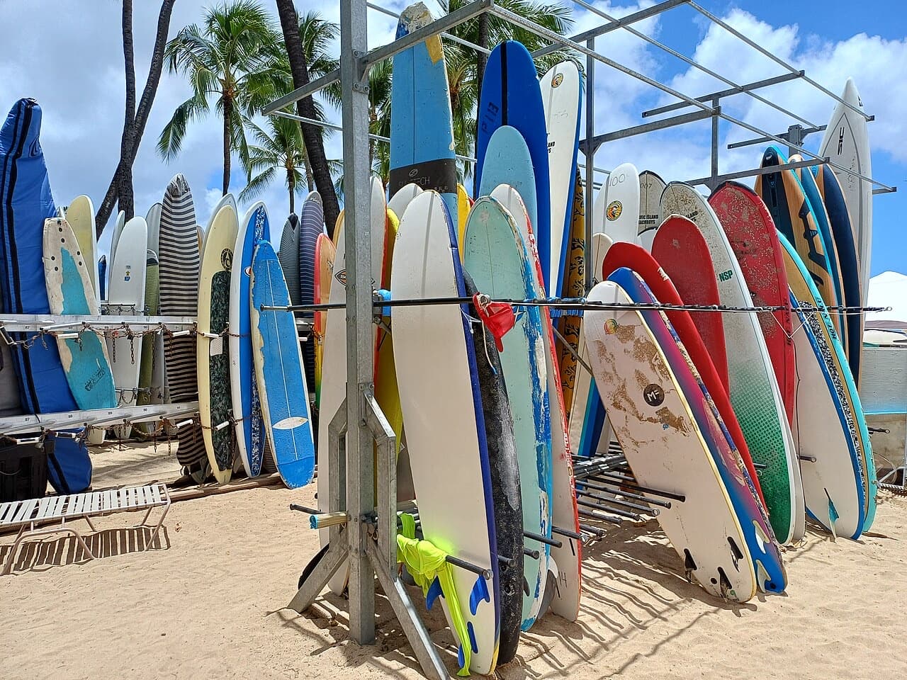 Rental longboards and soft-top surfboards standing in a rack on a sandy beach, fins visible