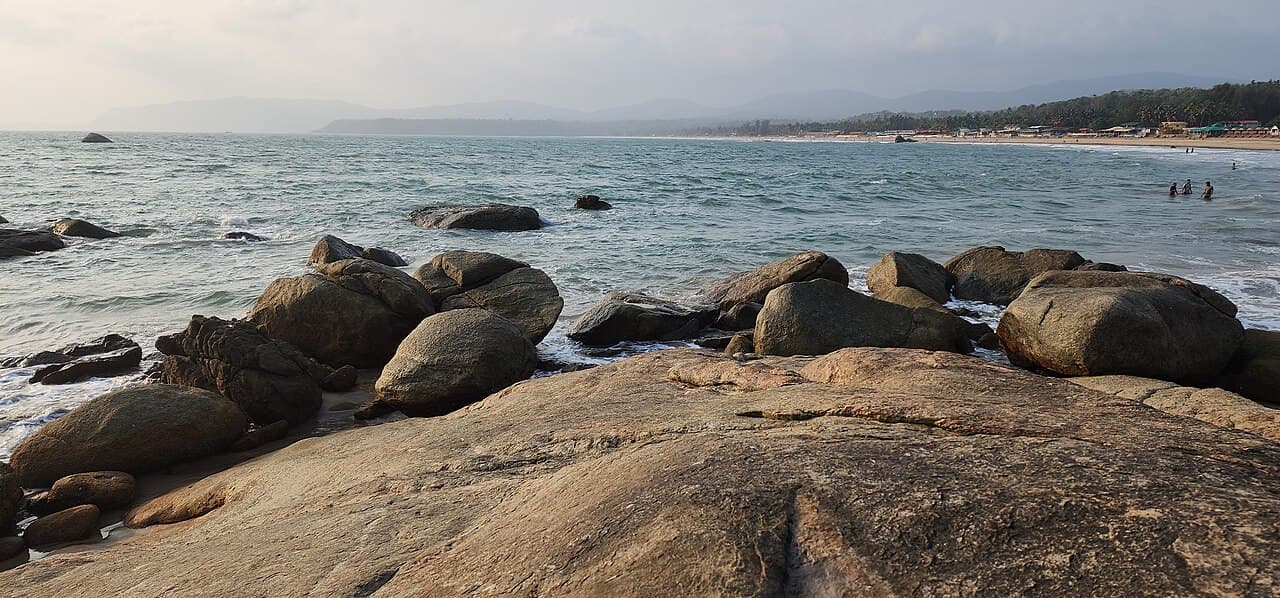 Large smooth boulders on Agonda Beach in evening light, with waves and a few swimmers in the distance