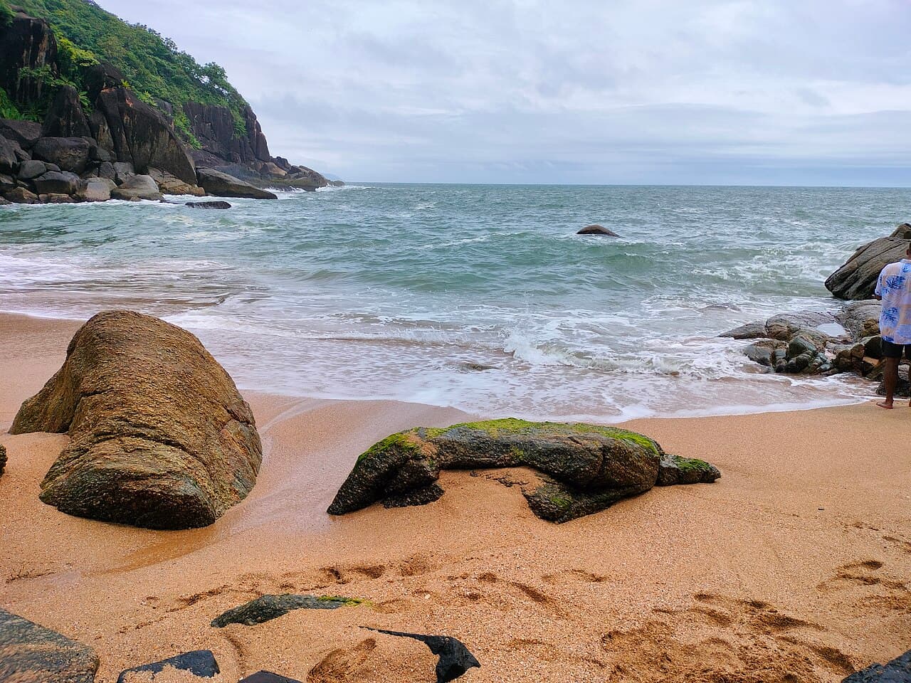 Mossy boulders on the sand at Butterfly Beach, with waves rolling in and a rocky wooded headland behind