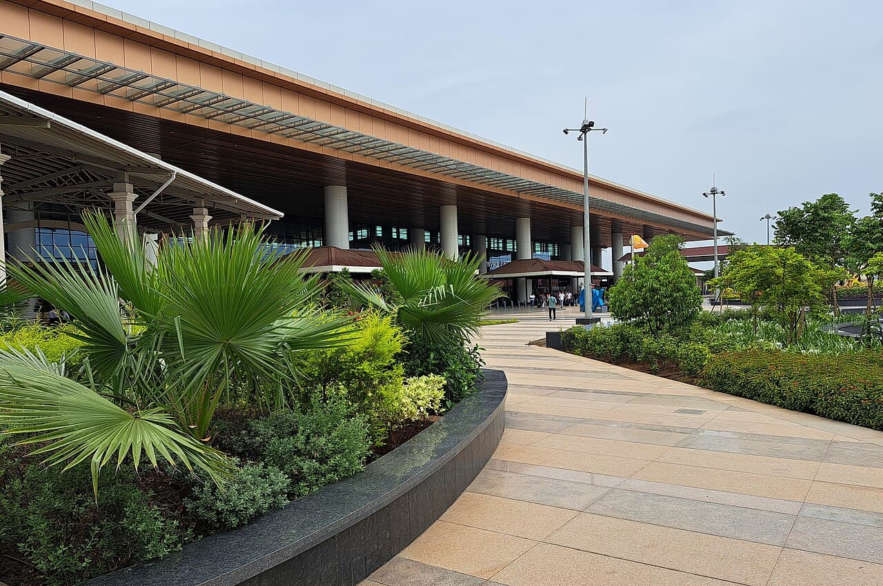 Exterior of Mopa airport terminal with a paved walkway lined by palms and landscaped planting beds