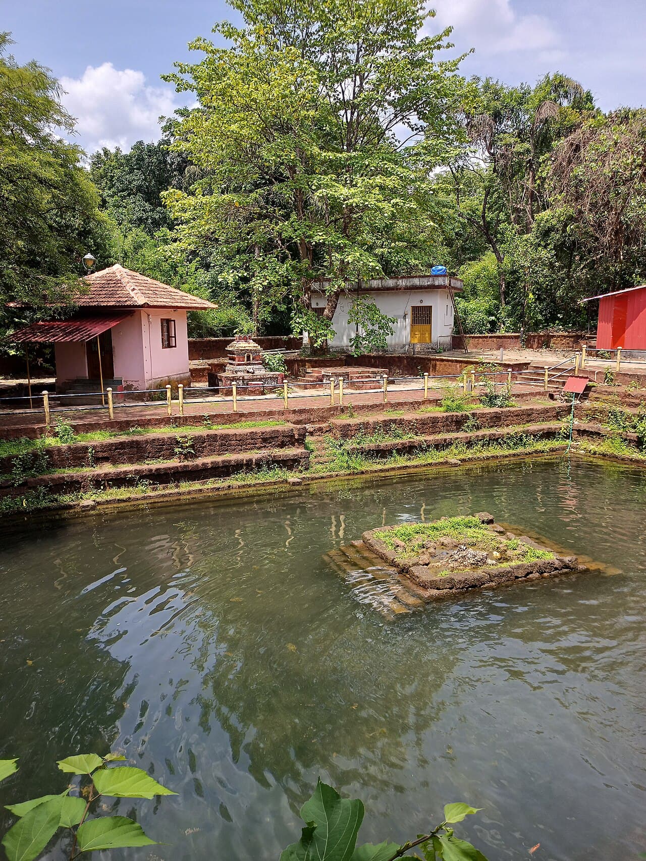 Budbudyanchi Tali, a stepped stone tank of green water with a small shrine and houses among trees
