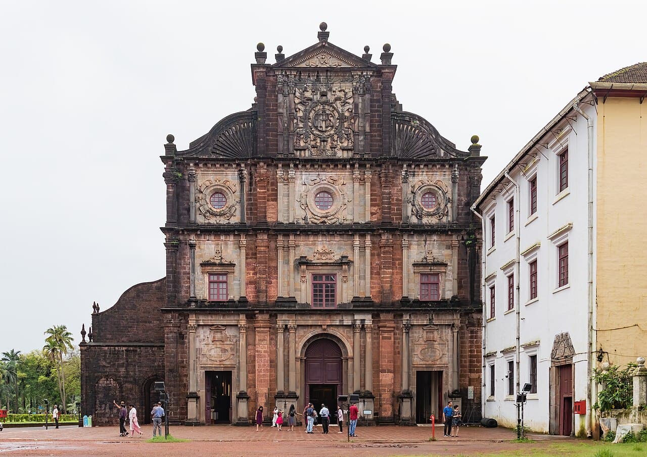 Carved stone and brick facade of the Basilica of Bom Jesus, with visitors walking in the square in front