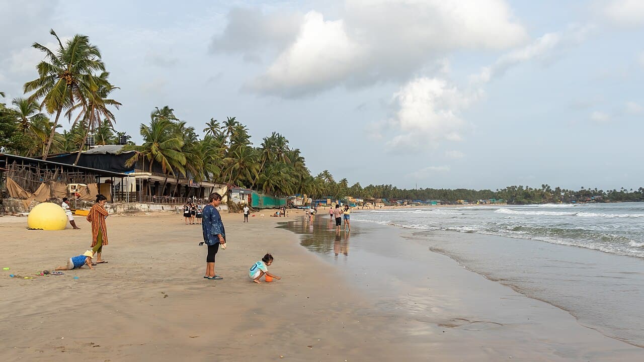 Palolem Beach with families playing on the sand, gentle waves and beach shacks under coconut palms