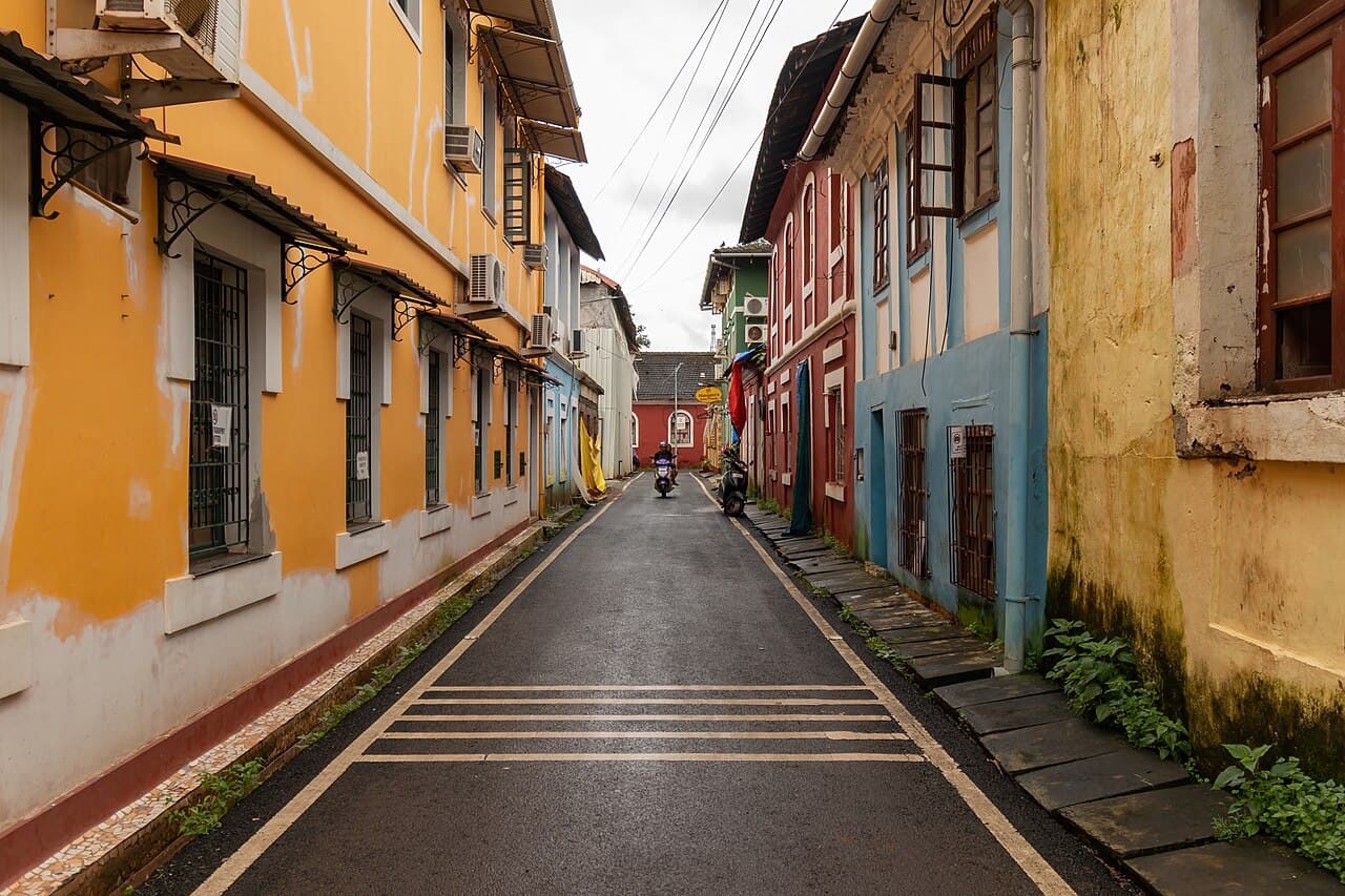A narrow wet street in Fontainhas, Panaji, lined with yellow, red and blue houses with balconies and window shades